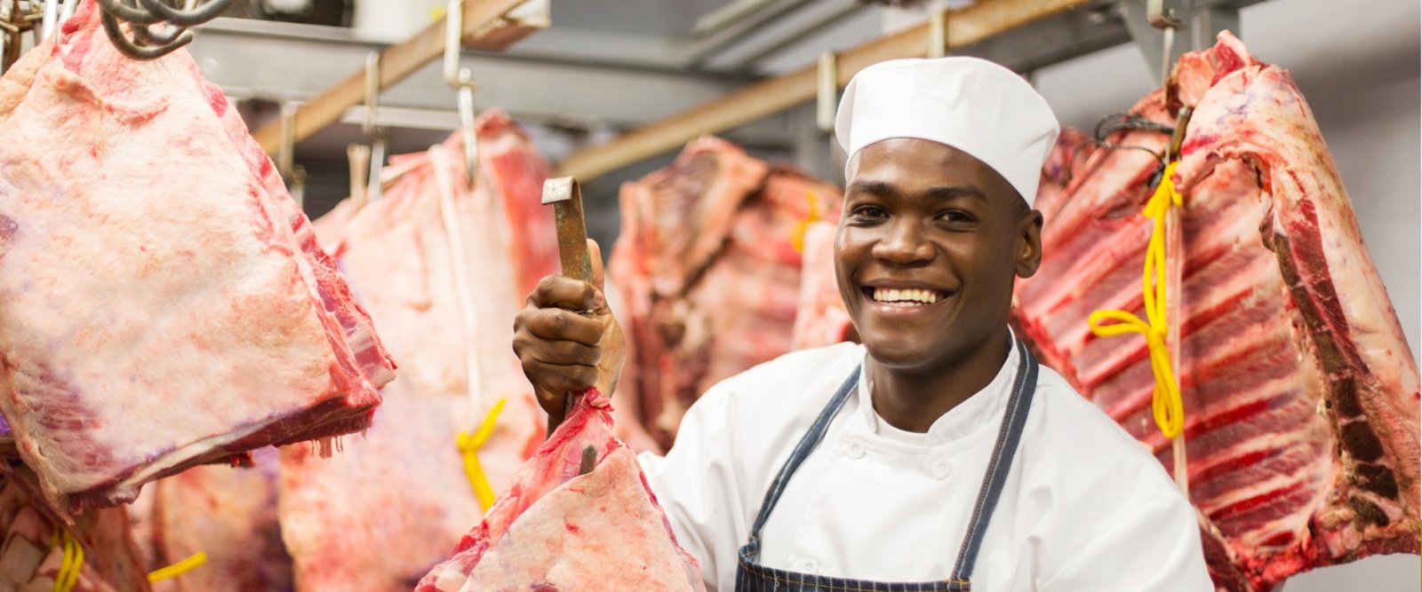 Butcher smiling in front of hanging cuts